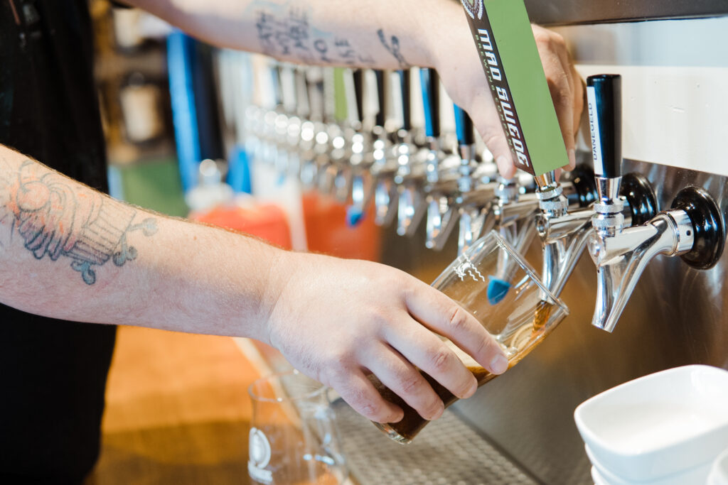 Hand holding glass pouring an India Pale Ale from a beer faucet into a glass.