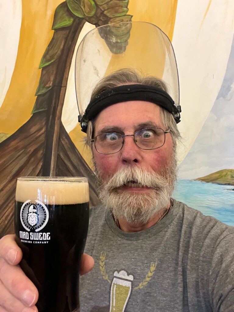 Brewer holding a glass of dark beer with a worried and challenged look on his face.